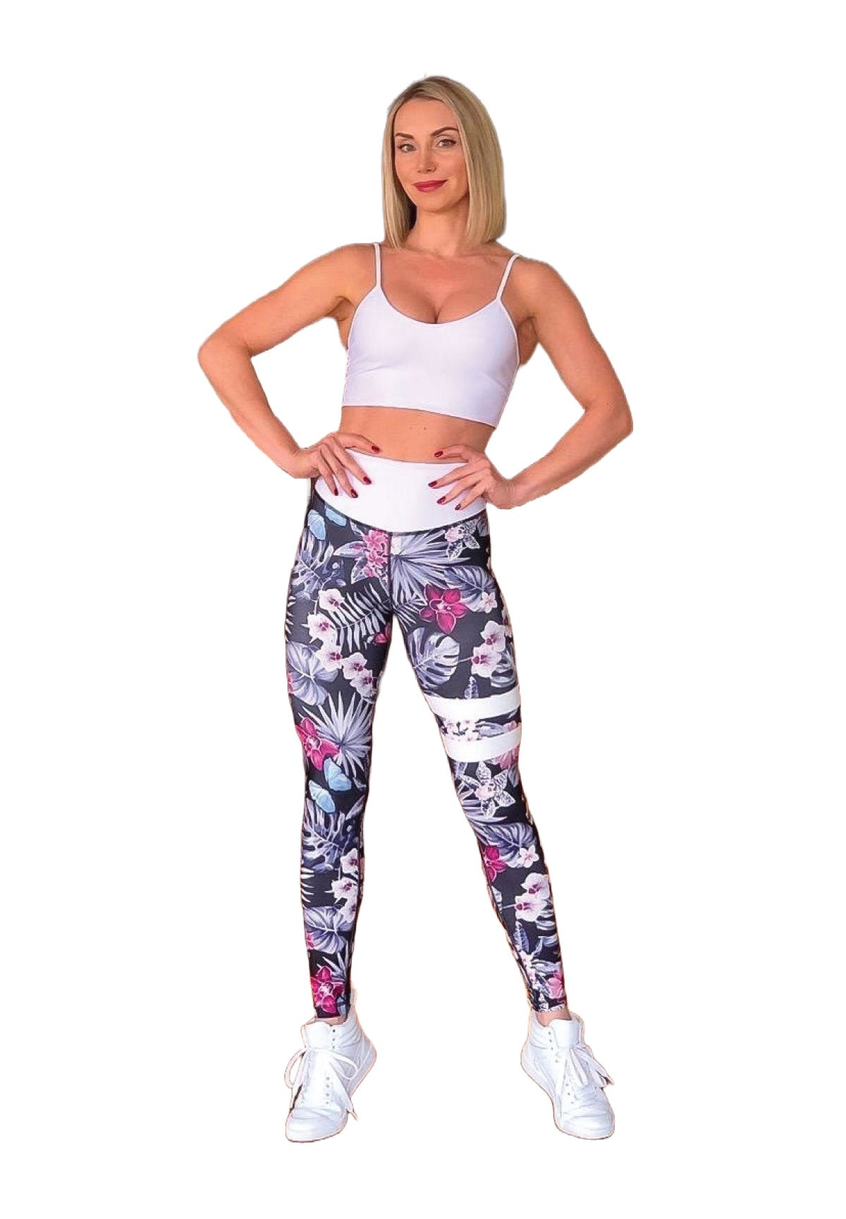 Frau in Lisminas weißem Sport-BH und geblumten Leggings 890 Extra High Waist Schwarz & Weiss, posiert selbstbewusst.